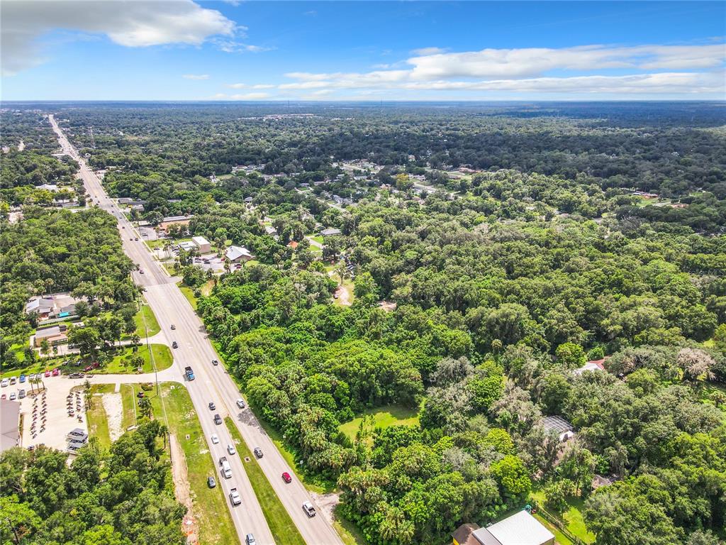 An aerial view shows a multi-lane highway running through a densely wooded residential area — 1351 N VOLUSIA AVENUE, ORANGE CITY, FL