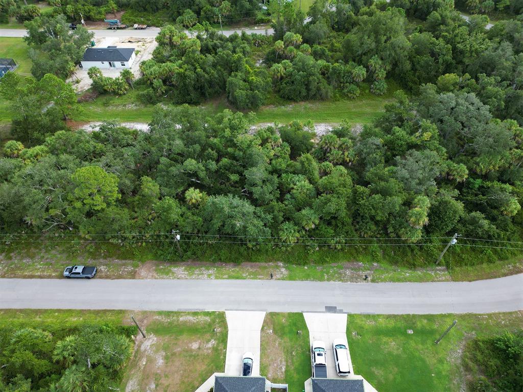 An aerial view shows a vacant, wooded lot situated across the street from residential homes — RHAPSODY AVENUE, NORTH PORT, FL