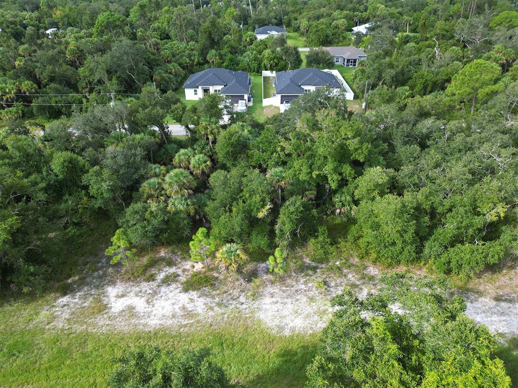 An aerial view shows a vacant, wooded lot in front of two modern residential homes — RHAPSODY AVENUE, NORTH PORT, FL