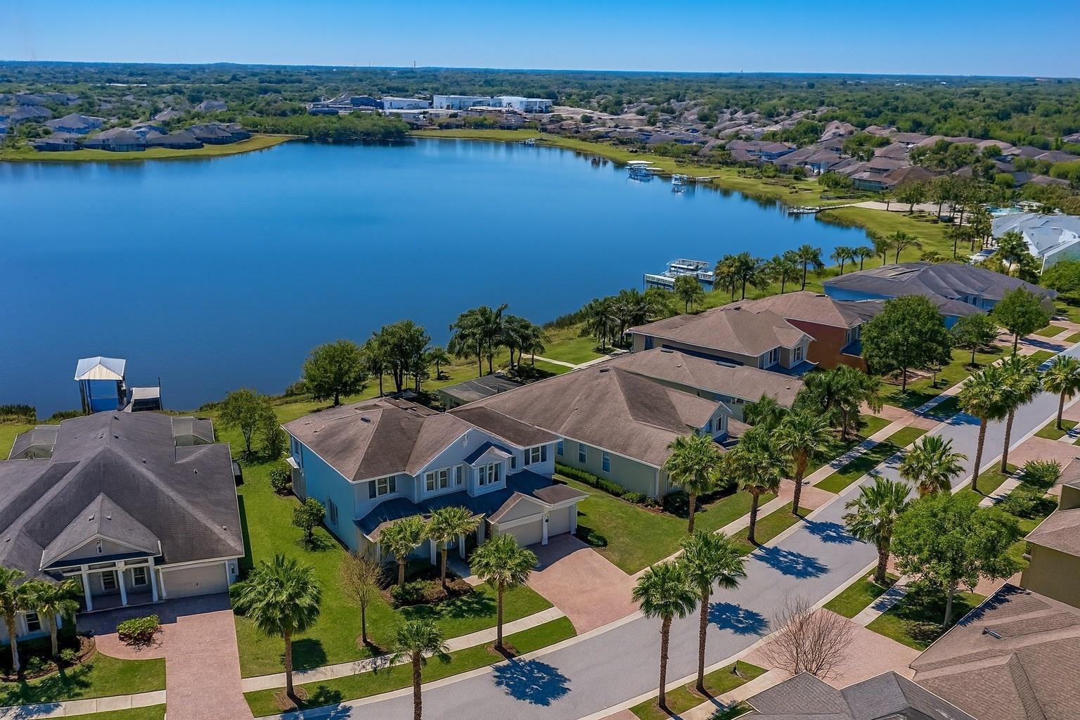 An aerial view shows waterfront suburban houses with palm trees along a paved street — 11333 Lake Lucaya Drive, FL 33579, FL