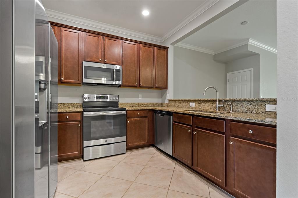 A kitchen features dark wood cabinets, granite countertops, stainless steel appliances, and tile flooring — 7275 KETCH PLACE, BRADENTON, FL
