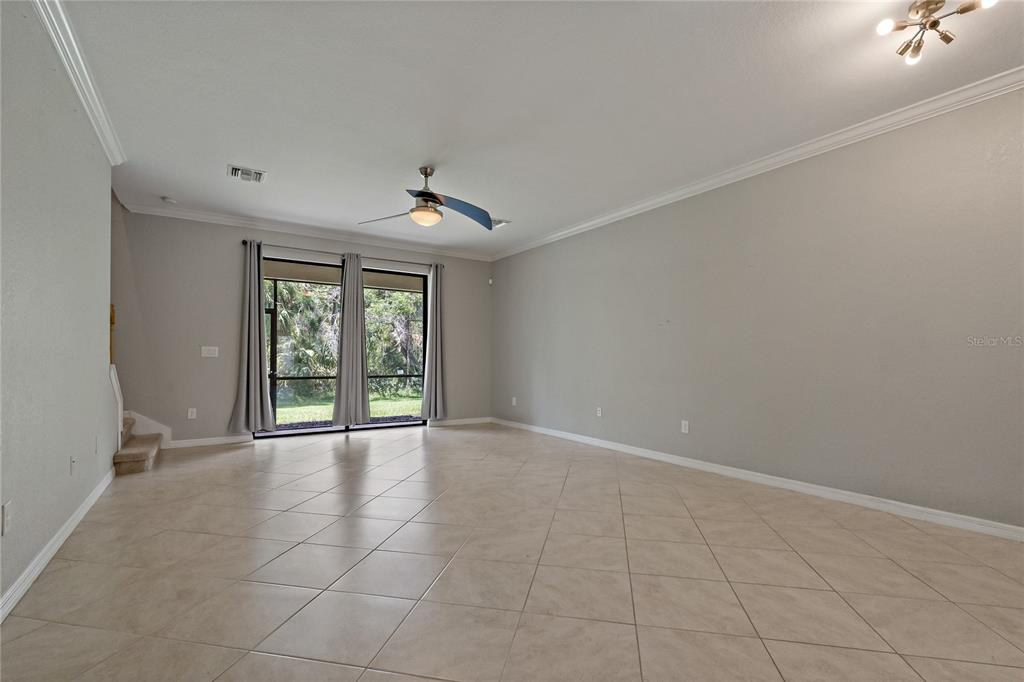 A spacious living room features light tile flooring, a ceiling fan, and sliding glass doors — 7275 KETCH PLACE, BRADENTON, FL