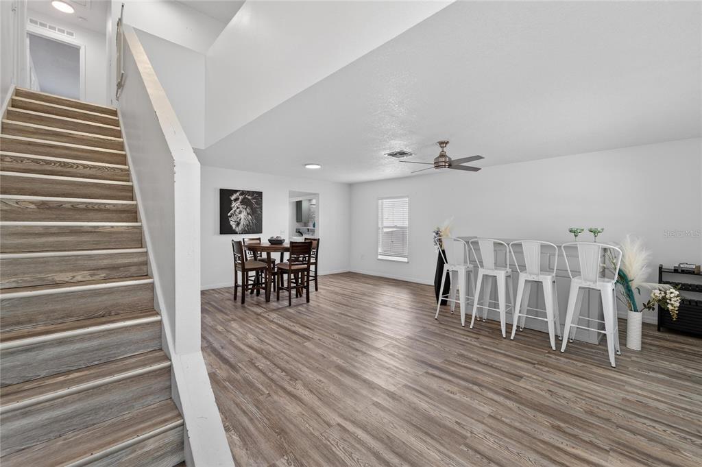 A bright room features wood-look flooring, a staircase, a dining set, and a breakfast bar — 10325 FROG POND DRIVE, RIVERVIEW, FL