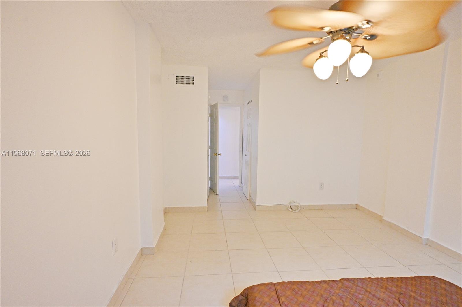 A room with white walls, tiled flooring, and a ceiling fan leads to a hallway — 947 Lenox Ave # 203, Miami Beach FL 33139, MIAMI BEACH, FL