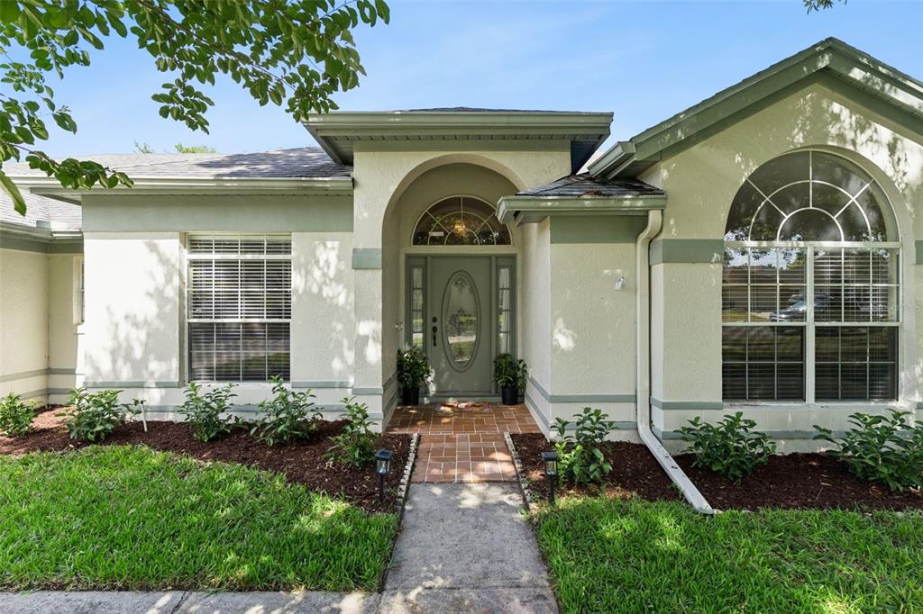 A single-story house exterior features a light-colored stucco facade, arched entryway, and a tiled walkway — 3883 KINGSTON OAKS COVE, OVIEDO, FL