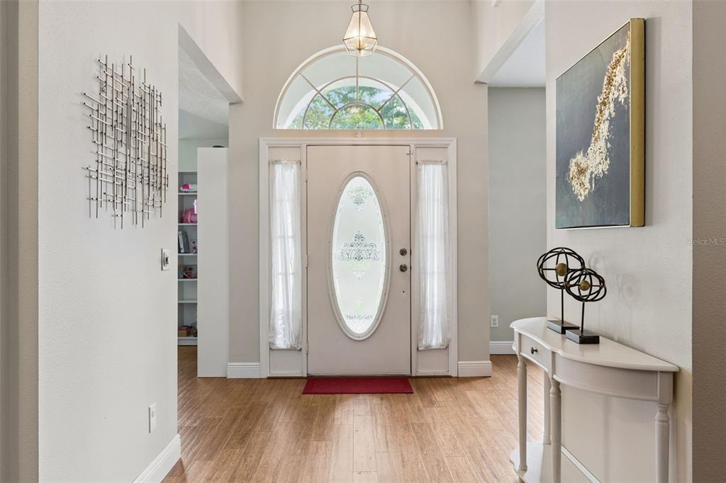 An entryway features a white front door with a glass insert, wood-look flooring, and decor — 3883 KINGSTON OAKS COVE, OVIEDO, FL