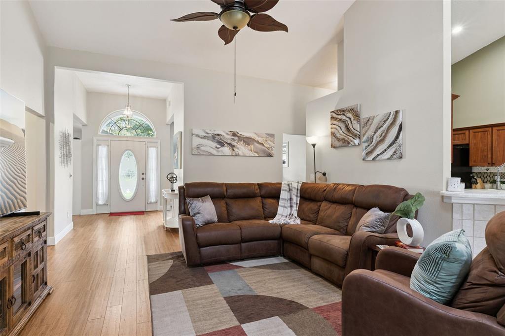 A living room features a brown sectional sofa, a patterned area rug, and wood flooring — 3883 KINGSTON OAKS COVE, OVIEDO, FL