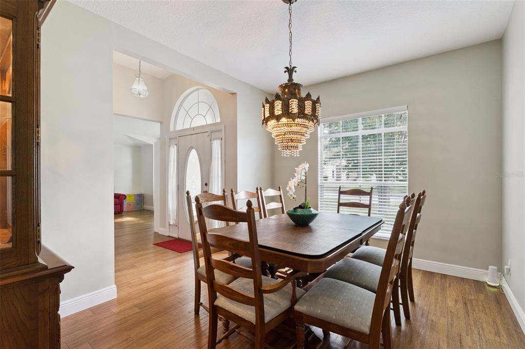 A dining room features a wooden table, chairs, a crystal chandelier, and hardwood flooring — 3883 KINGSTON OAKS COVE, OVIEDO, FL