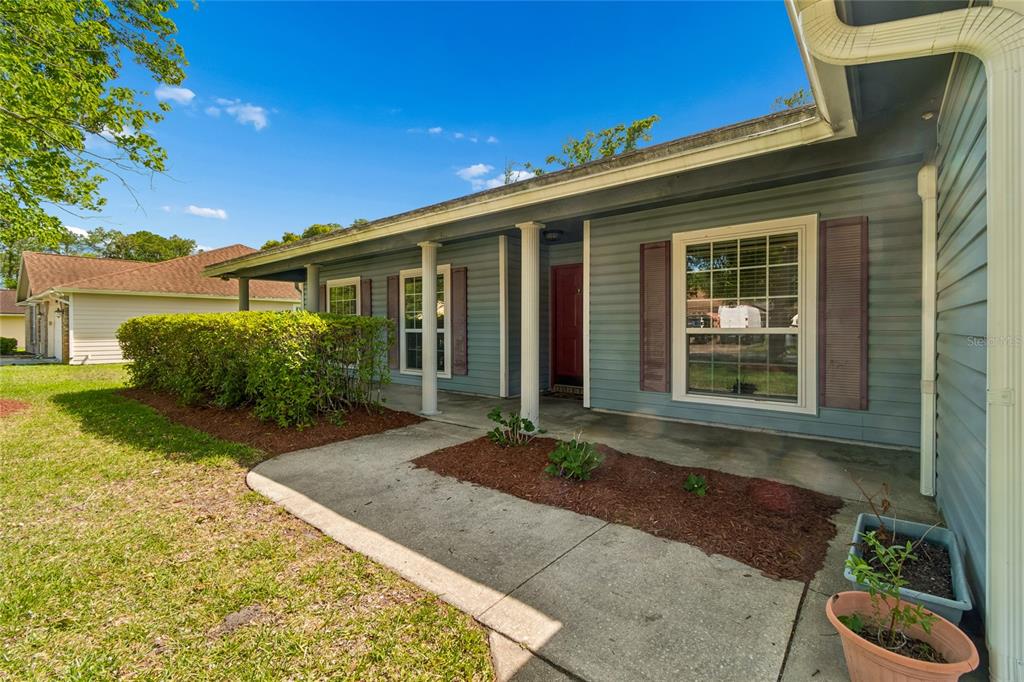 A blue-sided house with a covered front porch, white columns, and a red front door — 12160 BANYAN TREE DRIVE, JACKSONVILLE, FL