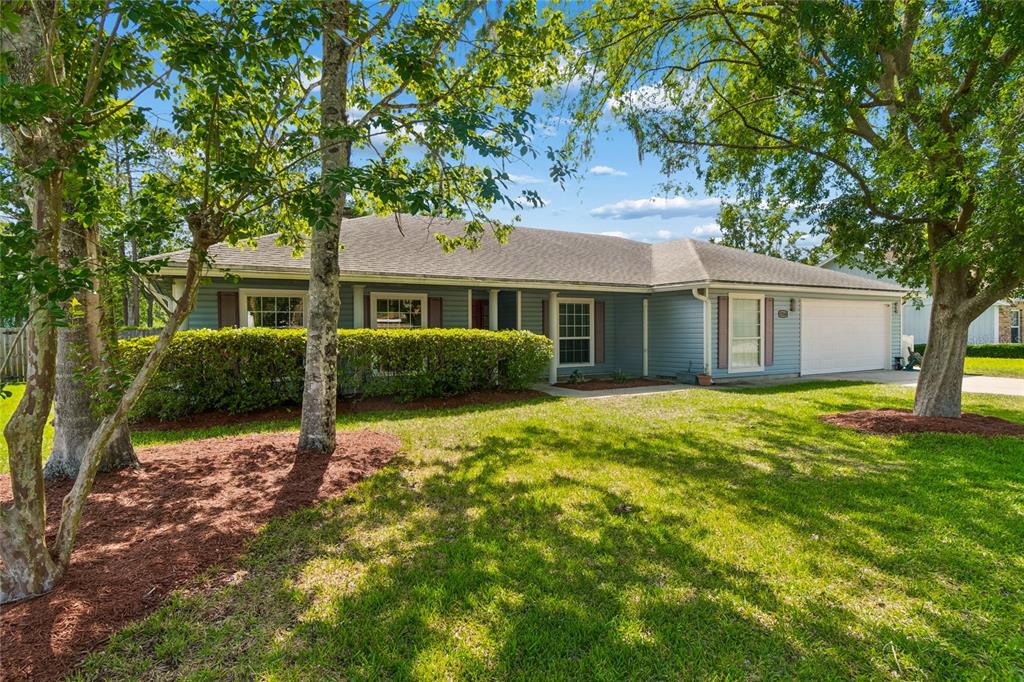 A single-story house with blue siding, a white garage door, and a landscaped front yard — 12160 BANYAN TREE DRIVE, JACKSONVILLE, FL