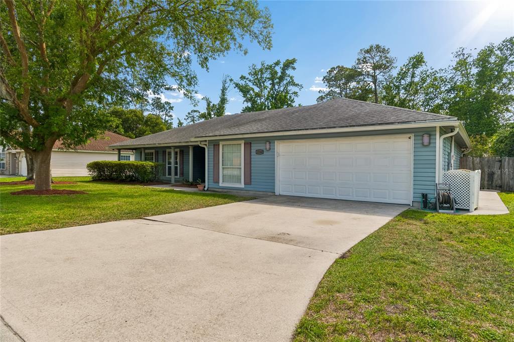 A single-story house with blue siding, a white garage door, and a concrete driveway — 12160 BANYAN TREE DRIVE, JACKSONVILLE, FL
