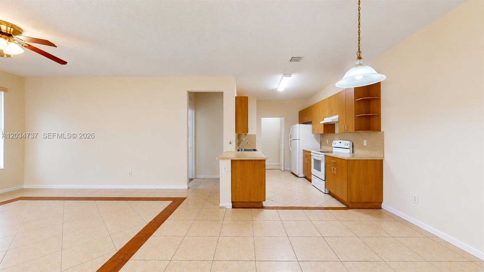 This kitchen features wood cabinets, white appliances, and tile flooring in an open floor plan — 3557 Forest Hill Blvd # 51, Palm Springs FL 33406, PALM SPRINGS, FL