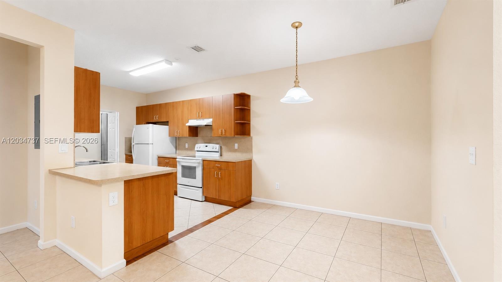 A kitchen features wood cabinets, white appliances, and a tile floor with an adjacent dining area — 3557 Forest Hill Blvd # 51, Palm Springs FL 33406, PALM SPRINGS, FL