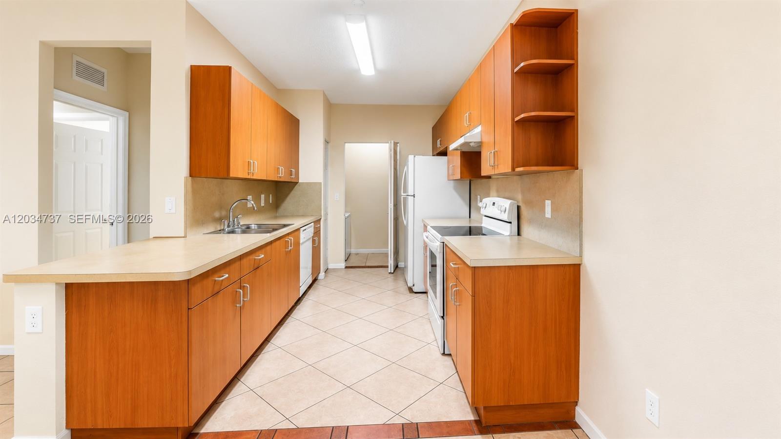 A galley kitchen features wood cabinets, light countertops, and tile flooring — 3557 Forest Hill Blvd # 51, Palm Springs FL 33406, PALM SPRINGS, FL