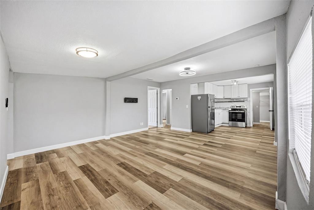 A living room with light gray walls and wood-look flooring opens into a kitchen area — 605 S S DISSTON AVE, TARPON SPRINGS, FL