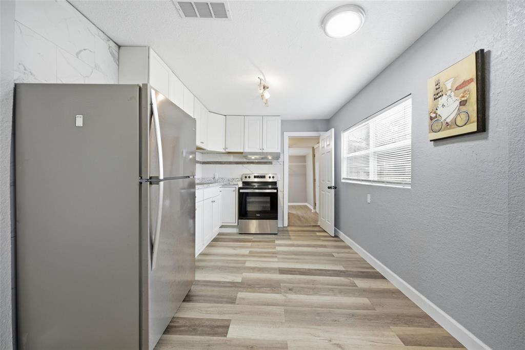 A kitchen features white cabinets, stainless steel appliances, gray walls, and wood-look flooring — 605 S S DISSTON AVE, TARPON SPRINGS, FL
