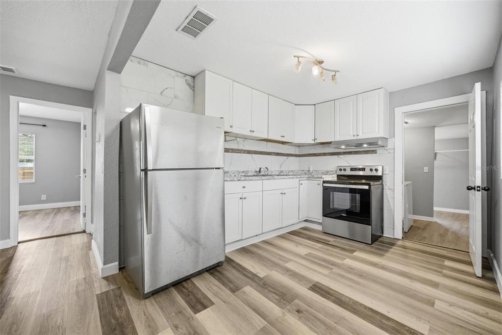 A kitchen with white cabinets, stainless steel appliances, marble-look backsplash, and wood-look flooring — 605 S S DISSTON AVE, TARPON SPRINGS, FL