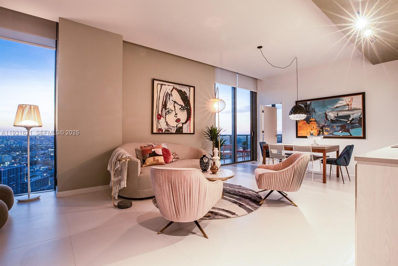 A modern living and dining area features pink velvet chairs, a curved sofa, and floor-to-ceiling windows — 501 NE 31st St, Miami FL 33137, MIAMI, FL