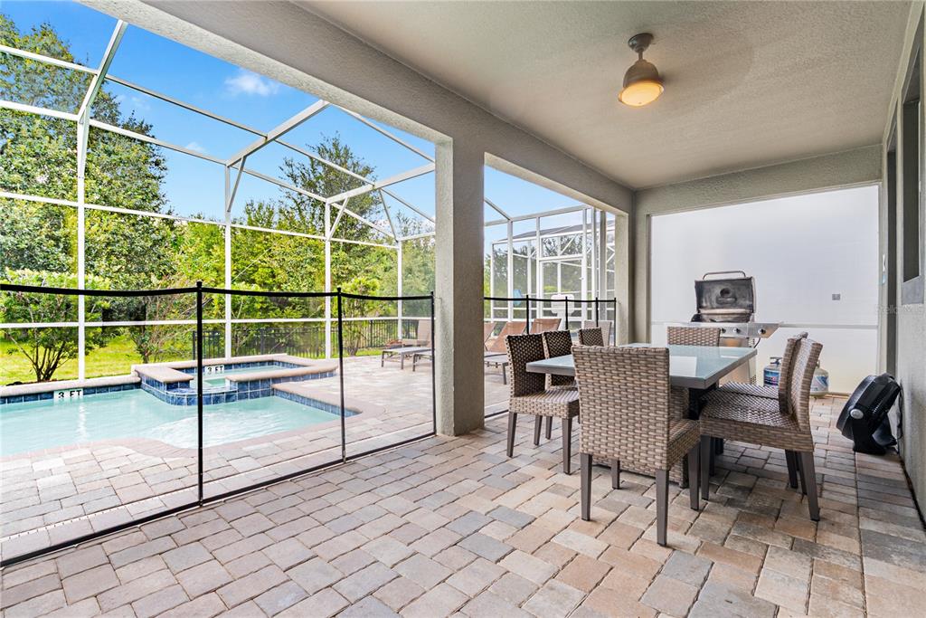 A covered patio features a dining set, a grill, and a screened-in pool area — 8809 CRUDEN BAY COURT, DAVENPORT, FL