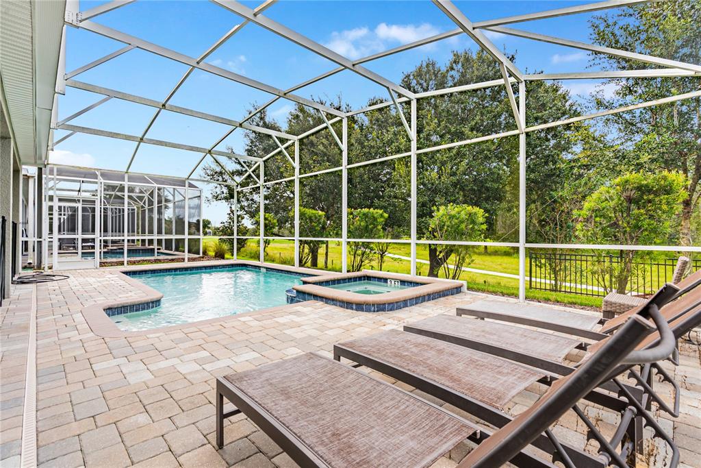 A screened-in pool and hot tub area with lounge chairs on a paved patio — 8809 CRUDEN BAY COURT, DAVENPORT, FL