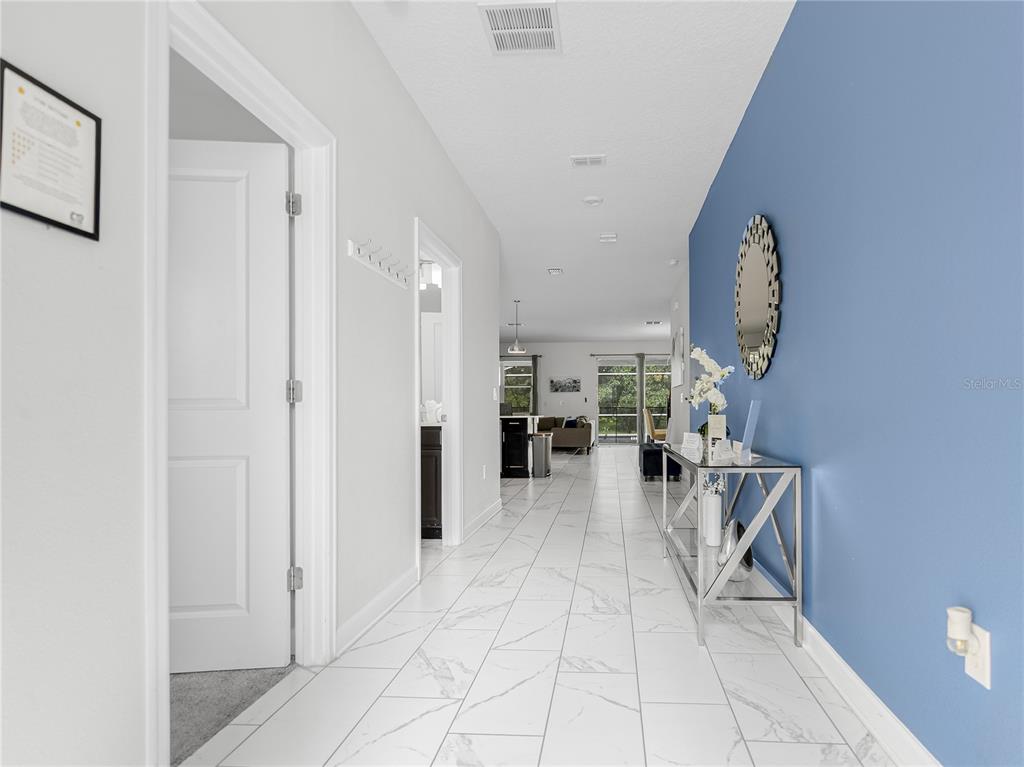 A hallway with white marble-look tile flooring leads to an open living area — 8809 CRUDEN BAY COURT, DAVENPORT, FL