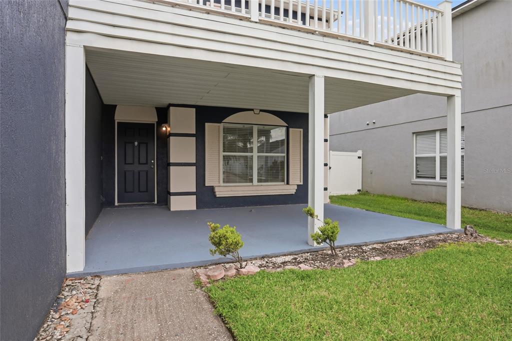 A covered concrete patio sits in front of a dark blue house with a balcony — 1161 KEMPTON CHASE PARKWAY, ORLANDO, FL