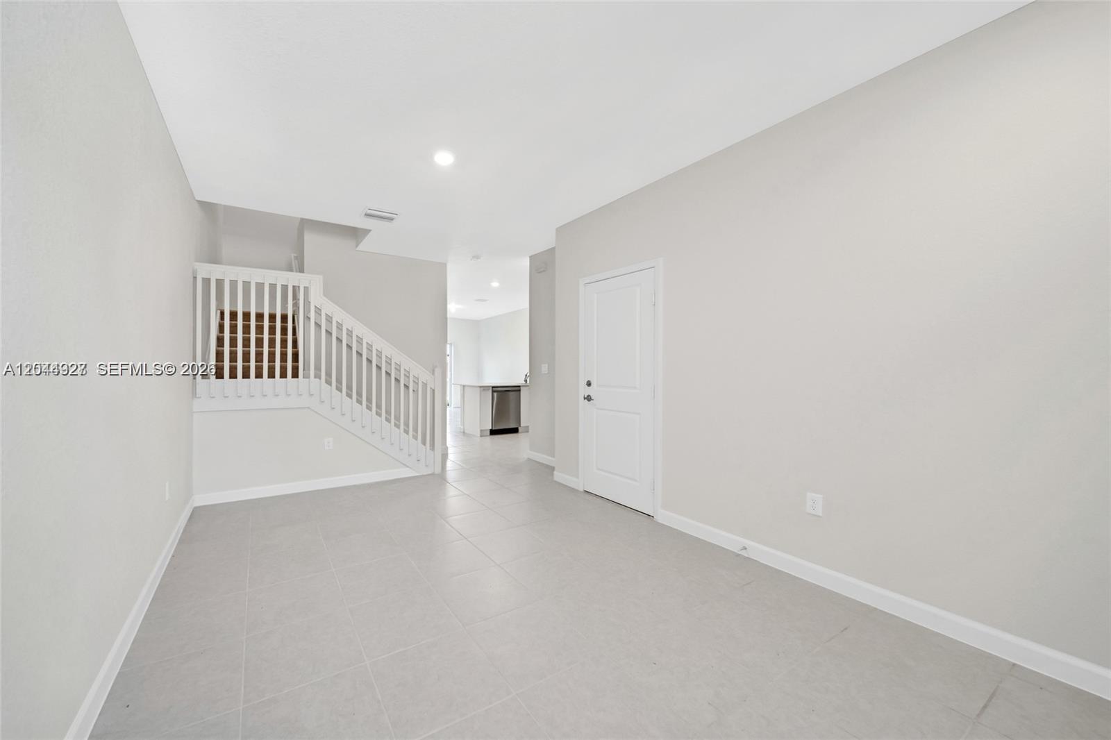 A room with light gray tile flooring, a white staircase, and a closed door — 12942 NW 23rd Pl, Miami FL 33167, MIAMI, FL