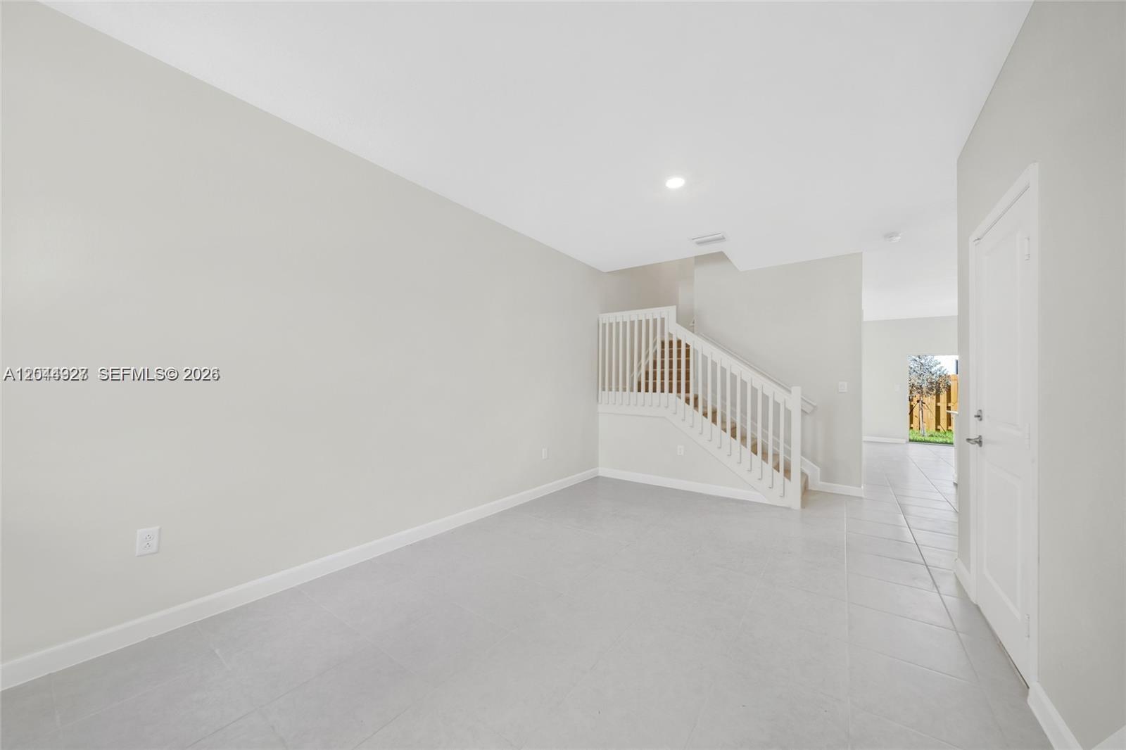 An empty room features light gray tile flooring, white walls, and a staircase with white railings — 12942 NW 23rd Pl, Miami FL 33167, MIAMI, FL