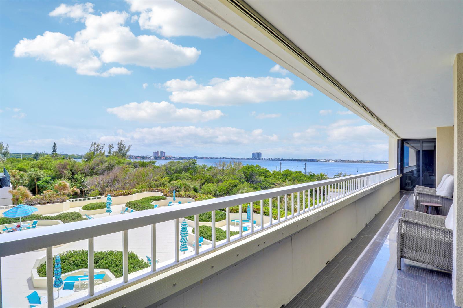 A balcony with a white railing overlooks a pool deck, lush trees, and a bay — 5280 N Ocean Drive # 2f, Riviera Beach FL 33404, RIVIERA BEACH, FL