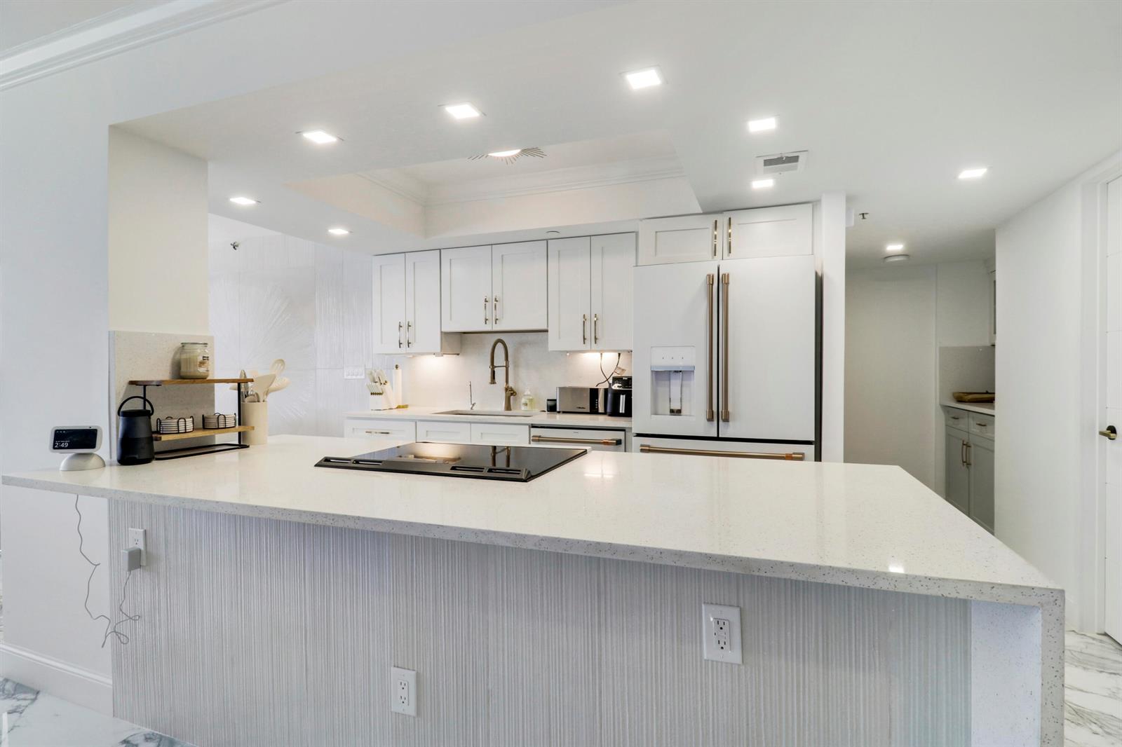 A modern white kitchen features a quartz-topped island with a cooktop and textured cabinetry — 5280 N Ocean Drive # 2f, Riviera Beach FL 33404, RIVIERA BEACH, FL