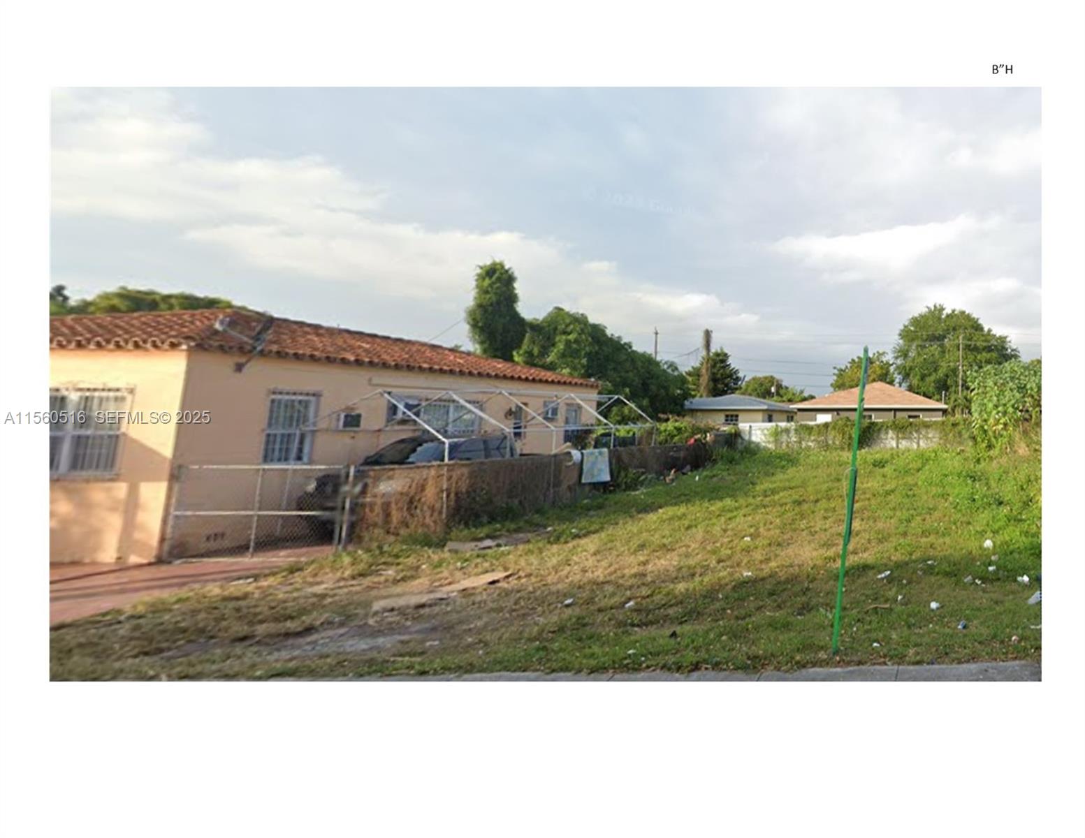 A tan house with a red tile roof sits next to an empty grassy lot — NW 62 STREET, Miami FL 33147, MIAMI, FL