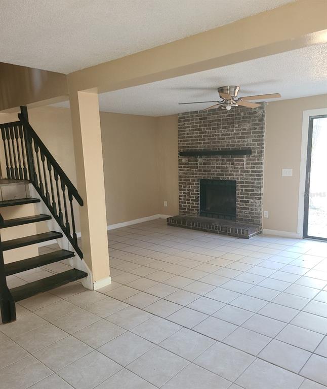 A living room features a brick fireplace, tile flooring, and a staircase with black railings — 4910 SILVER OAKS VILLAGE UNIT B, ORLANDO, FL