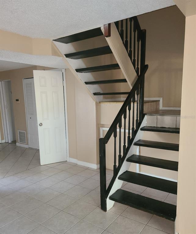 A staircase with black treads and railings stands in a room with tiled floors — 4910 SILVER OAKS VILLAGE UNIT B, ORLANDO, FL