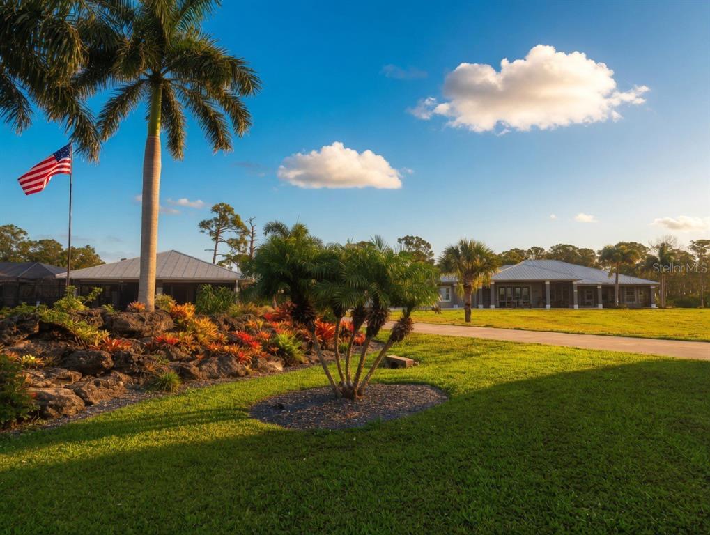 A grassy yard features a palm tree, a flag, and two houses under a blue sky — 9150 DEER COURT, VENICE, FL