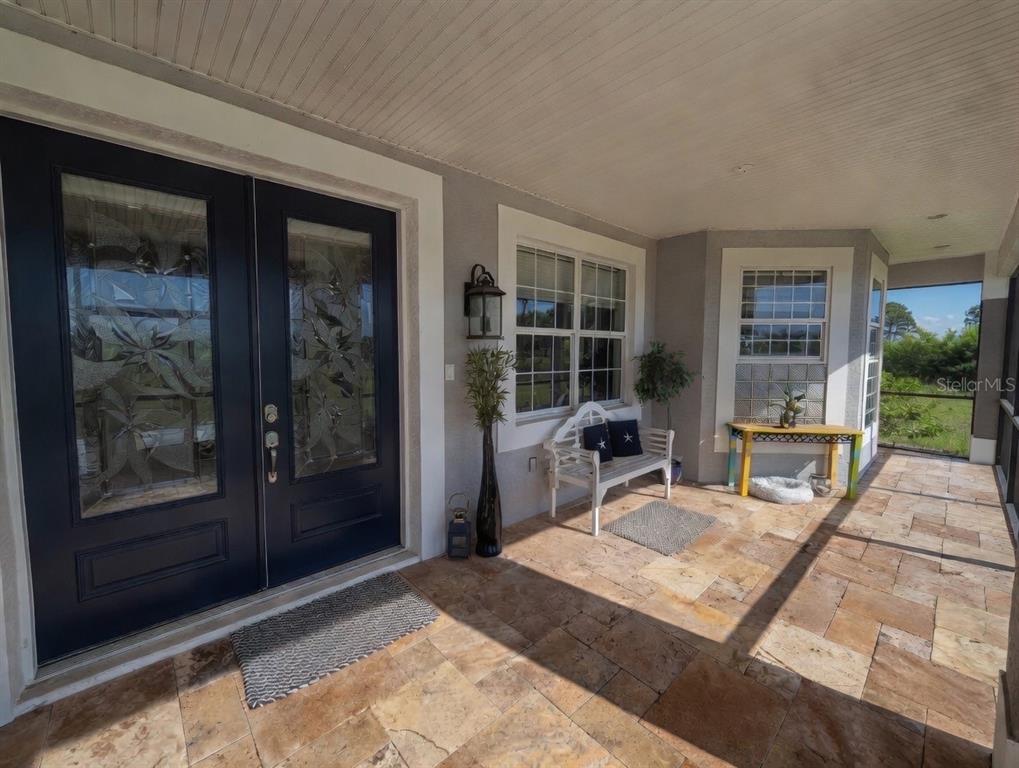 A covered front porch features stone tile flooring, a dark double door, and a white bench — 9150 DEER COURT, VENICE, FL
