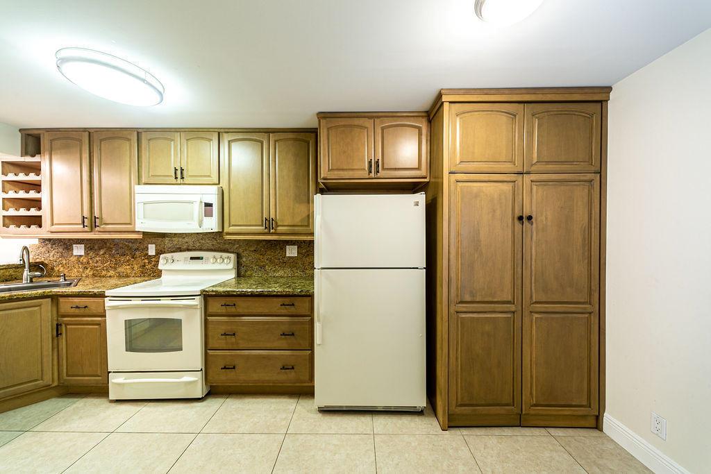 A kitchen features wood cabinets, granite countertops, a white stove, and a white refrigerator — 6 Royal Palm Way # 102, Boca Raton FL 33432, BOCA RATON, FL