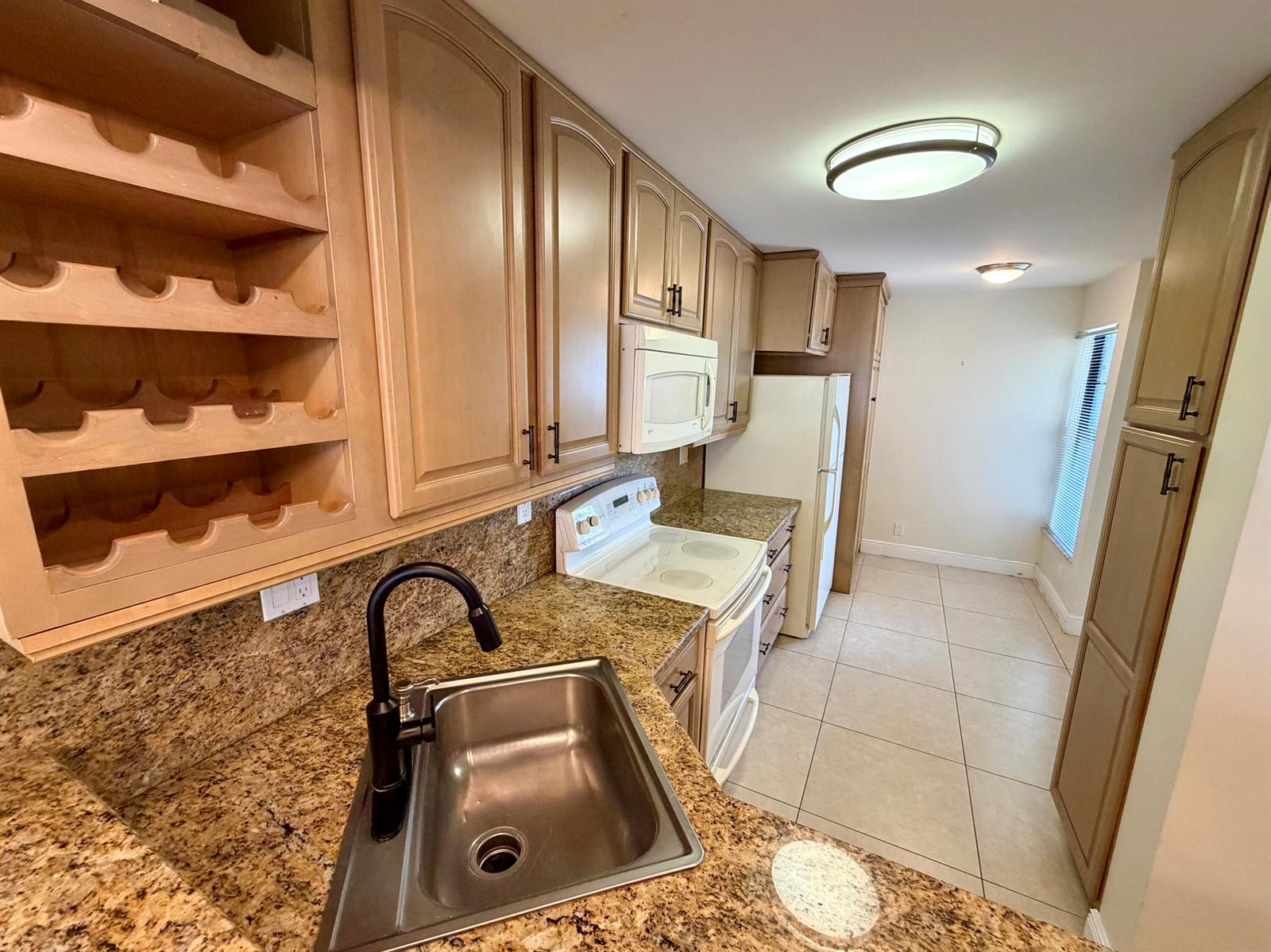 A kitchen features light wood cabinets, granite countertops, a stainless steel sink, and tile flooring — 6 Royal Palm Way # 102, Boca Raton FL 33432, BOCA RATON, FL