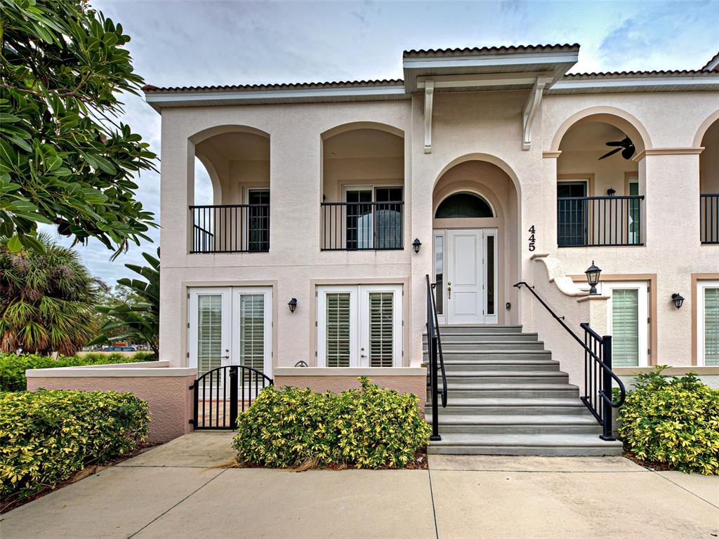 A two-story stucco building features a central staircase leading to an arched front entrance — 445 NOKOMIS AVENUE S UNIT 210, VENICE, FL