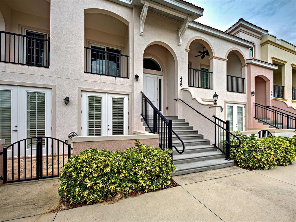 A multi-story townhouse exterior features arched entryways, black metal railings, and a concrete staircase — 445 NOKOMIS AVENUE S UNIT 210, VENICE, FL
