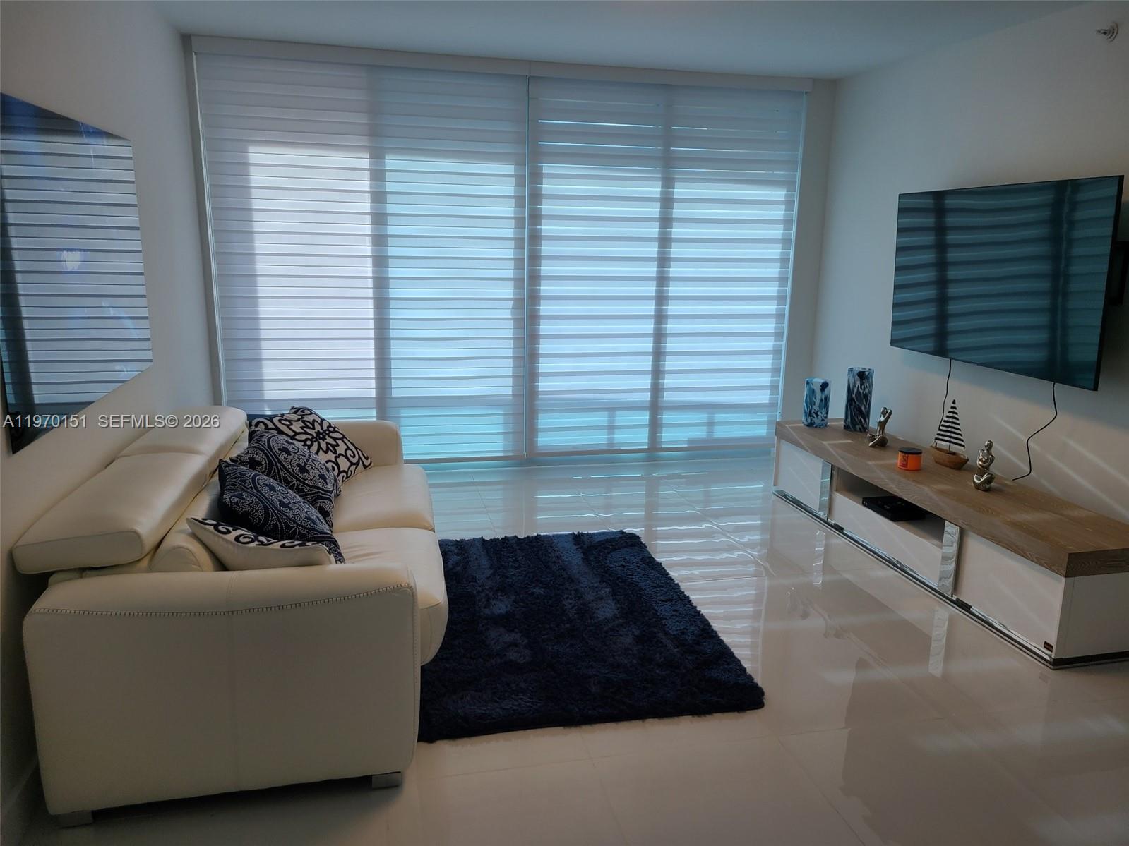 A living room features a white sofa, a dark rug, and a wall-mounted television — 2501 S Ocean Dr # 1031, Hollywood FL 33019, HOLLYWOOD, FL