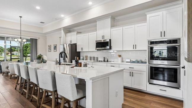 A modern kitchen features white cabinetry, a large island with bar seating, and stainless appliances — 30653 PRESTWICK AVENUE, SORRENTO, FL