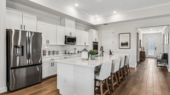 A modern kitchen features white cabinetry, stainless steel appliances, a large island, and hardwood floors — 30653 PRESTWICK AVENUE, SORRENTO, FL