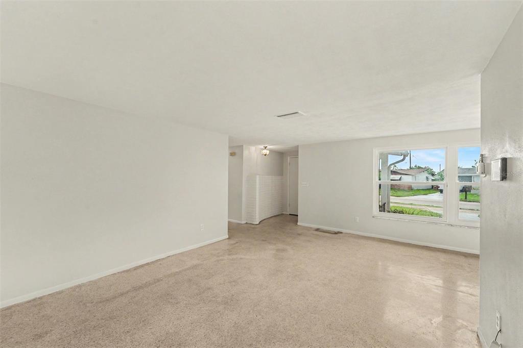 An empty living room features beige carpeting, light gray walls, and a large window — 3536 KIMBERLY OAKS DRIVE, HOLIDAY, FL