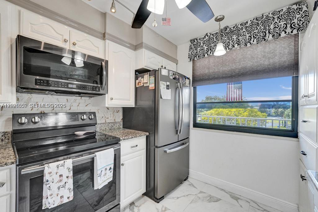 A kitchen features white cabinetry, stainless steel appliances, marble-look flooring, and a window with blinds — 1502 Whitehall Dr # 305, Davie FL 33324, DAVIE, FL