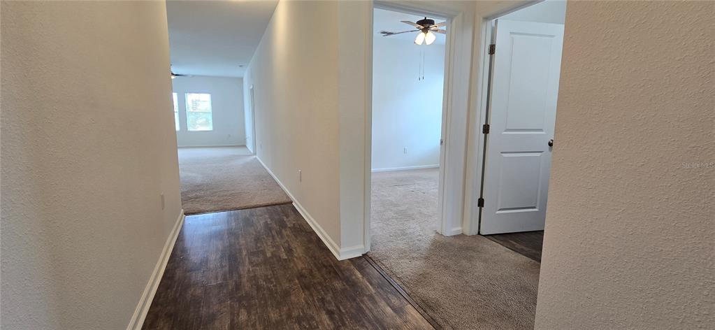 A hallway with wood-look flooring leads to carpeted rooms and a white interior door — 15660 MERLIN AVENUE, MASCOTTE, FL