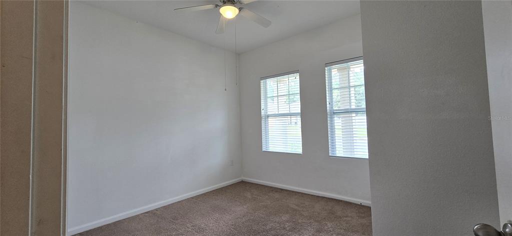 An empty room with white walls, brown carpet, two windows, and a ceiling fan — 15660 MERLIN AVENUE, MASCOTTE, FL