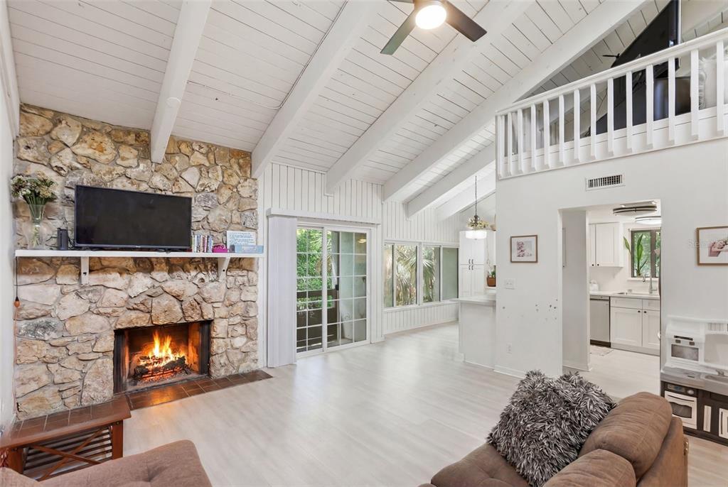 A living room features a stone fireplace, vaulted ceilings, and a view into the kitchen — 200 FAIRWAY DRIVE UNIT 200, LONGWOOD, FL