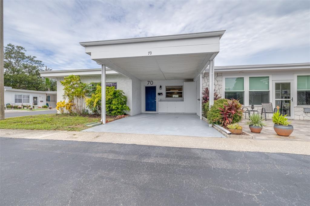 A single-story home features a blue front door, a covered carport, and a paved patio — 13940 ANONA HEIGHTS DRIVE UNIT 70, LARGO, FL