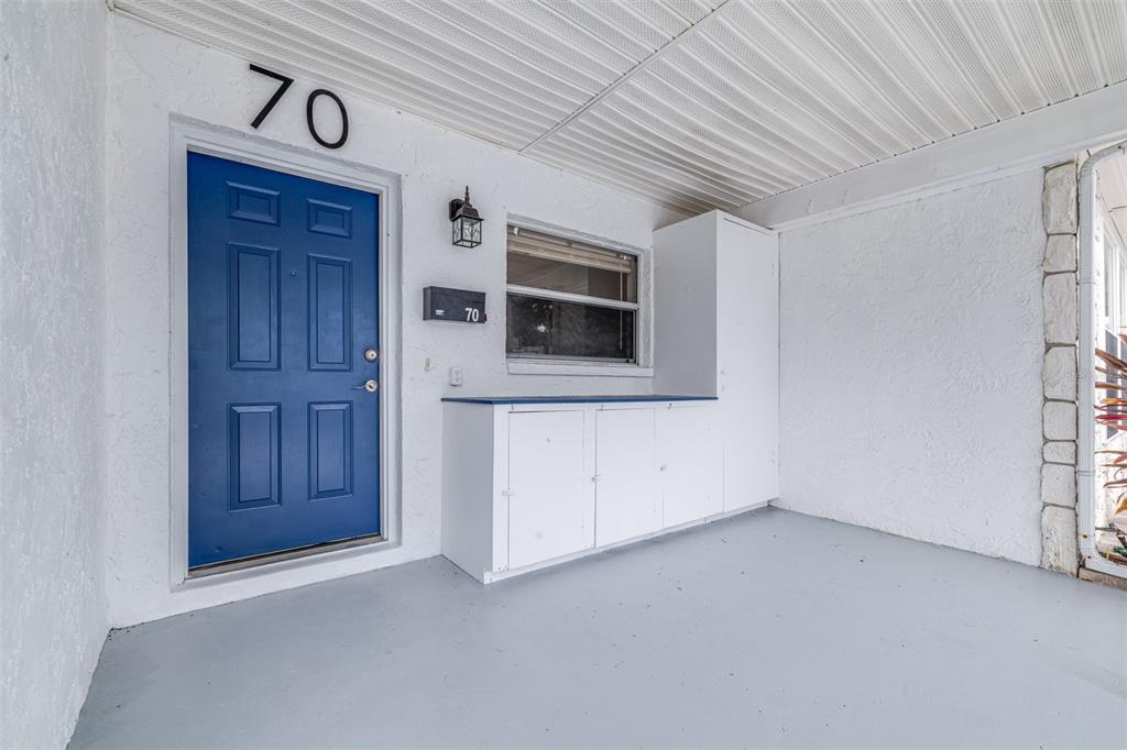 A covered porch features a blue front door, white cabinets, and a gray floor — 13940 ANONA HEIGHTS DRIVE UNIT 70, LARGO, FL