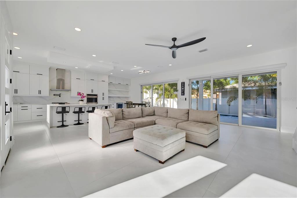 A bright, open-concept living room and kitchen with white cabinetry, tile floors, and sliding doors — 3723 NORWOOD COURT, SARASOTA, FL